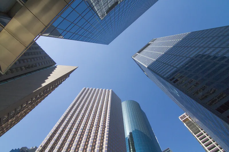 Glass office towers converging overhead against a clear blue sky in TX