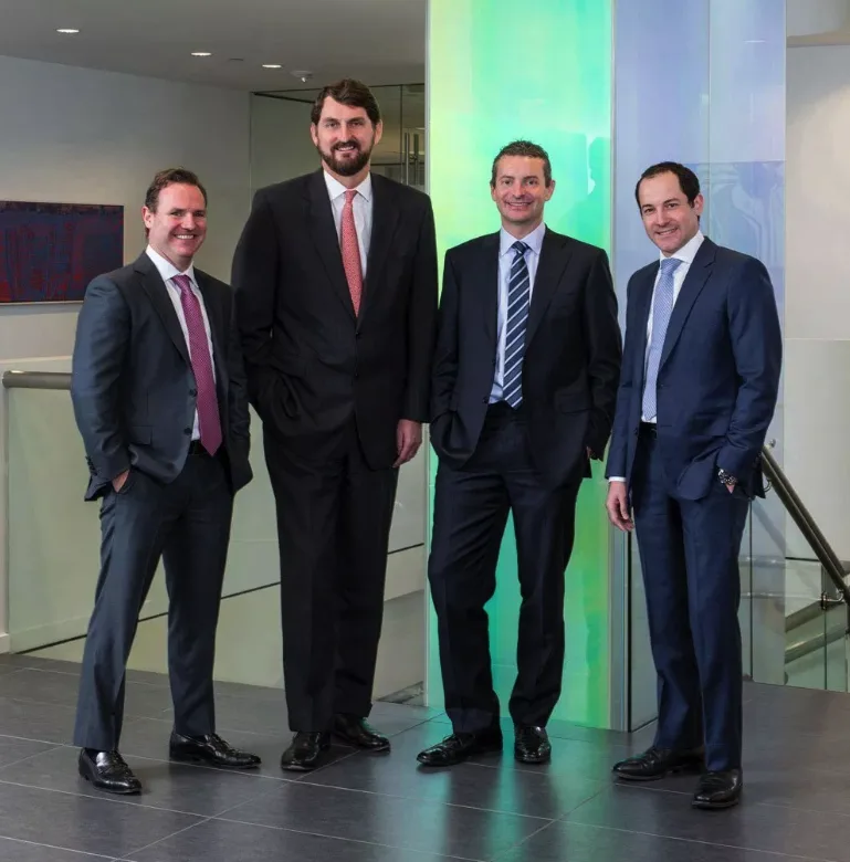 group executive portrait four professionals dark suits modern office lobby