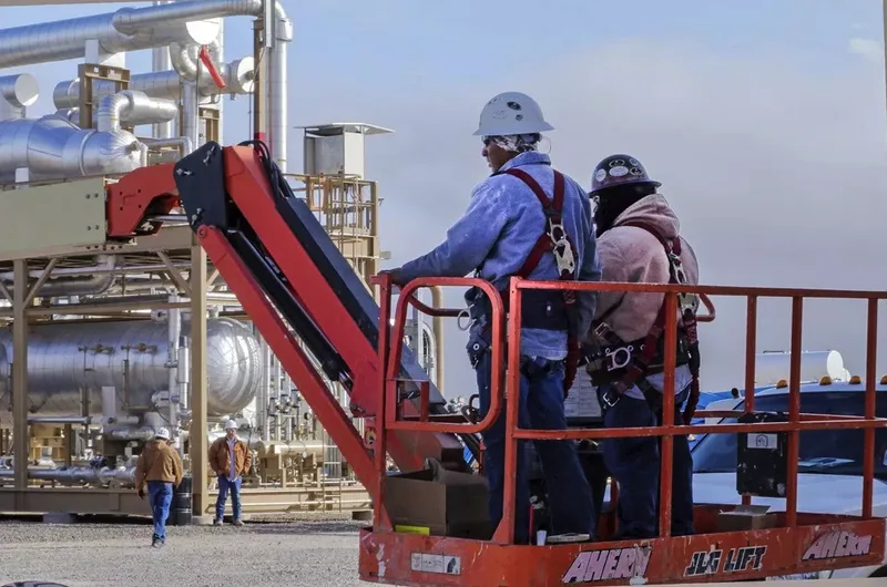 workers in safety harnesses on boom lift at industrial processing facility