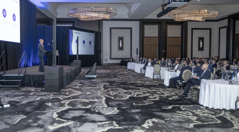 Executive speaker addressing seated corporate audience under elegant ballroom chandeliers