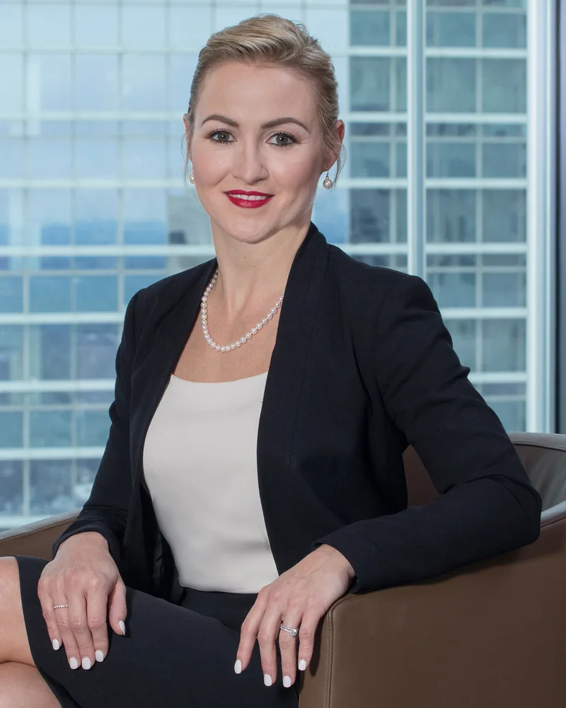Executive headshot of professional woman in blazer, pearl necklace, high-rise backdrop
