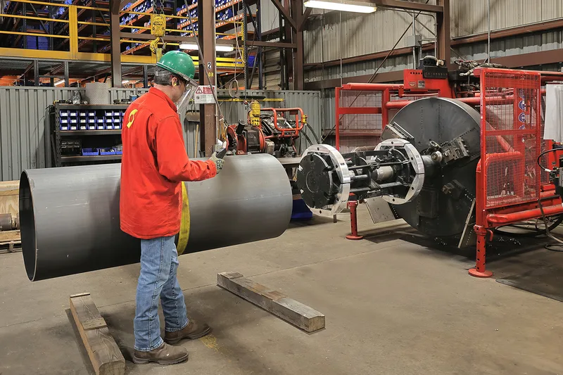 Industrial location worker guiding large-diameter black steel pipe into beveling machine