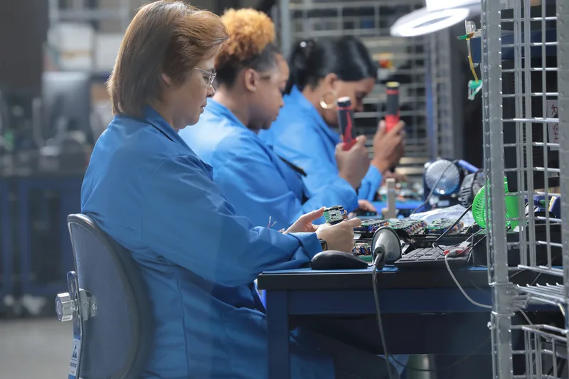 electronic assembly line workers hand-inspecting circuit boards under bright factory lamps