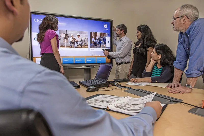 Corporate lifestyle team gathered around conference table reviewing large screen presentation