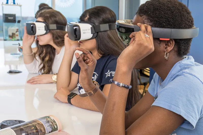 three women wearing Gear VR and HoloLens mixed reality headsets at white table